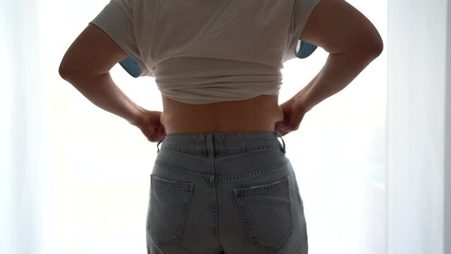 Back view. Close-up of fatty deposits at the waist. Girl in jeans of small size, hanging down the sides