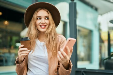 Young blonde girl using smartphone and drinking coffee at the city.