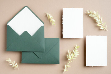 Rustic wedding stationery set top view. Green envelope, blank white paper cards, dried flowers on pastel beige background. Flat lay, top view, copy space.