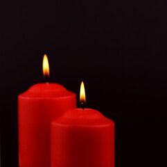 Two red burning candles on black