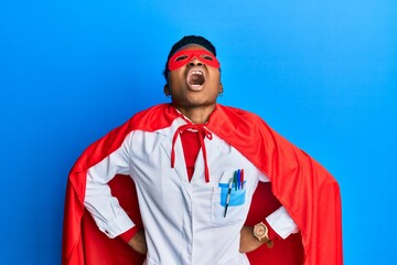 Young african american woman wearing doctor uniform and super hero costume angry and mad screaming frustrated and furious, shouting with anger looking up.