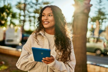 Young latin woman smiling happy using touchpad at the city.