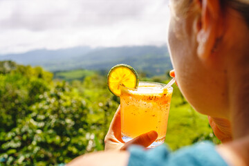Woman drinking a michelada in front of a forest landscape.