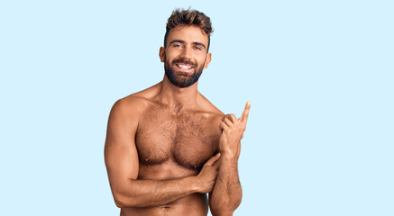Young hispanic man wearing swimwear shirtless with a big smile on face, pointing with hand and finger to the side looking at the camera.