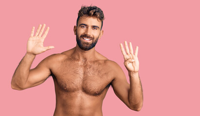 Fototapeta premium Young hispanic man wearing swimwear shirtless showing and pointing up with fingers number nine while smiling confident and happy.