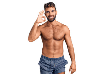 Fototapeta premium Young hispanic man wearing swimwear shirtless smiling positive doing ok sign with hand and fingers. successful expression.