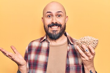 Young handsome man holding chickpeas bowl celebrating achievement with happy smile and winner expression with raised hand