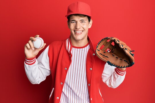 Handsome caucasian man wearing baseball uniform holding golve and ball smiling with a happy and cool smile on face. showing teeth.