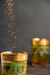 Close-up of glass of mint tea, with brown sugar falling, selective focus, on dark wooden table, dark background, vertical, with copy space