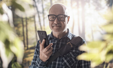 Fototapeta premium Happy man connecting in the forest with his smartphone