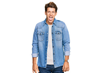 Fototapeta premium Handsome caucasian man wearing casual denim jacket sticking tongue out happy with funny expression. emotion concept.