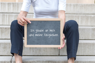 Eine Frau mit einer Tafel auf der eine Affirmation Ich glaube an mich und meine Fähigkeiten steht