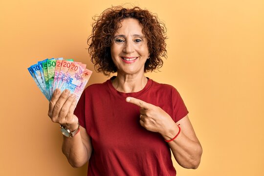 Beautiful middle age mature woman holding swiss franc banknotes smiling happy pointing with hand and finger