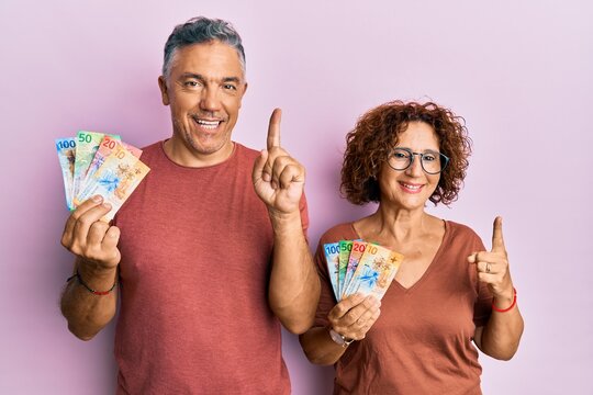 Beautiful middle age couple together holding swiss franc banknotes smiling with an idea or question pointing finger with happy face, number one