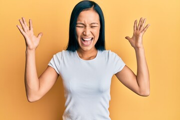 Beautiful hispanic woman wearing casual white tshirt celebrating mad and crazy for success with...