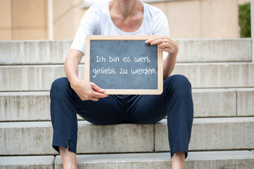Eine Frau mit einer Tafel auf der eine Affirmation Ich bin es wert geliebt zu werden steht