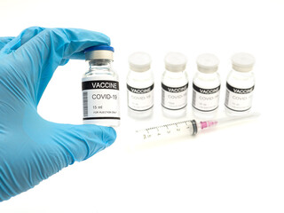 Hand holding a Covid-19 vaccine in a glass bottle with vaccine bottles and a syringe placed on a white background. Vaccine for prevention, immunization, and treatment from coronavirus infection