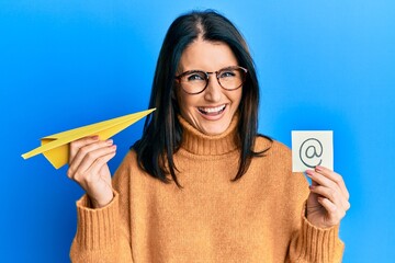 Middle age brunette woman holding email symbol and paper plane smiling and laughing hard out loud...
