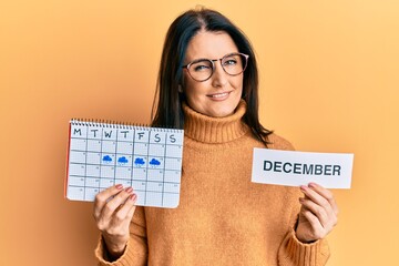 Middle age brunette woman holding december calendar winking looking at the camera with sexy...