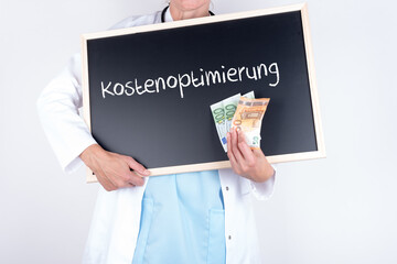Ärztin in einer Arztpraxis mit einer Tafel auf der Kostenoptimierung steht und mit einigen...