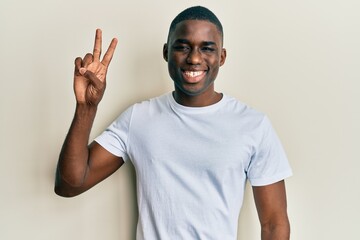 Young african american man wearing casual white t shirt smiling with happy face winking at the camera doing victory sign. number two.