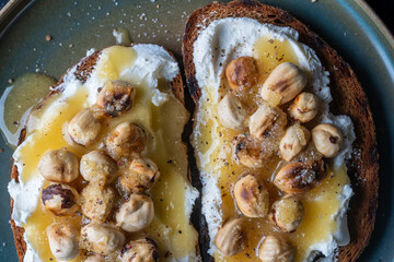Two bread toast with cream cheese, roasted hazelnuts, honey, pepper and salt, close up, top view