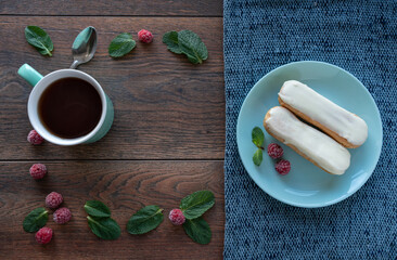 
Dessert ingredients. Food background. Mint leaves, fresh raspberries, a cup of tea, eclairs on a plate.