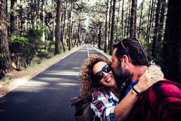 Happy young adult travel couple together with love and friendship enjoy the road and walking in the nature woods forest - selfie and woman smile hugging man in relationship adventure outdoor