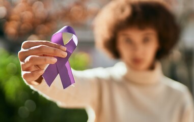 Young hispanic girl with serious expression holding purple awareness ribbon at the city. - Powered by Adobe