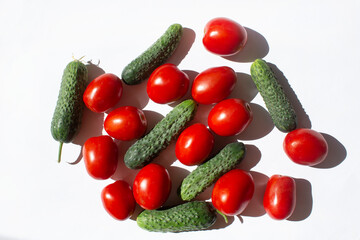 Green cucumbers and red tomatoes  on white sunny home kitchen table background top view 