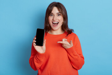 Portrait of surprised woman in casual clothing showing blank screen of mobile phone isolated over...