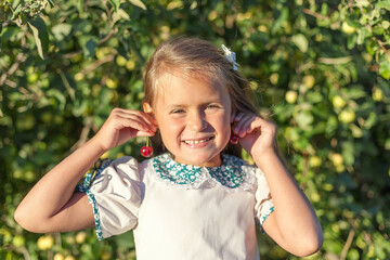 Portrait of child in apple orchard. Little girl in pink shirt and denim skirt, holding apples in her hands like ears