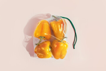 Reusable packaging of products by weight. Yellow bell peppers in a reusable bag on a pink background