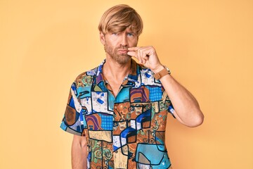 Young blond man wearing summer shirt mouth and lips shut as zip with fingers. secret and silent,...