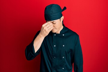 Handsome young man wearing professional cook uniform and hat tired rubbing nose and eyes feeling...