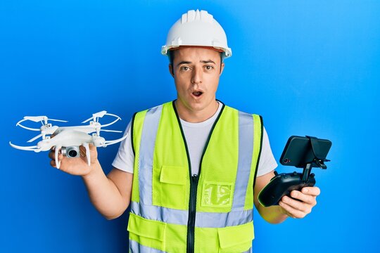 Handsome young man wearing safety hard using drone and control afraid and shocked with surprise and amazed expression, fear and excited face.