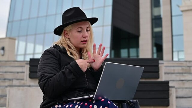 Young woman speaks sign language on a video call on a laptop outdoors. The deaf-mute girl communicates with gestures