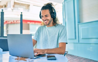 Fototapeta na wymiar Young hispanic man smiling happy working using laptop and headphones at terrace of coffee shop.