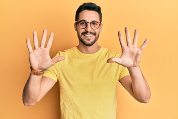Fototapeta premium Young hispanic man wearing casual clothes and glasses showing and pointing up with fingers number ten while smiling confident and happy.