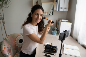 Confident young female beauty vlogger influencer record commercial content makeup tools video review on phone webcam. Capable young woman doing visage using brushes shoot master class on smartphone