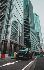 London UK January 2021 Vertical shot of a modern hybrid london taxi passing by on leadenhall street, massive tall skyscrapers reaching up high in the background. Street empty during covid lockdown