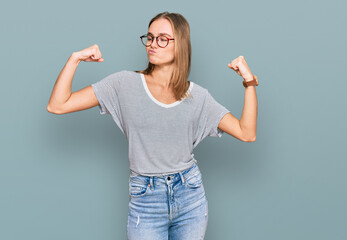 Beautiful young blonde woman wearing casual clothes and glasses showing arms muscles smiling proud. fitness concept.