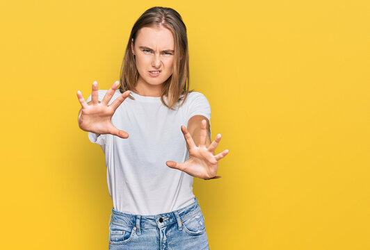 Beautiful young blonde woman wearing casual white t shirt doing stop gesture with hands palms, angry and frustration expression