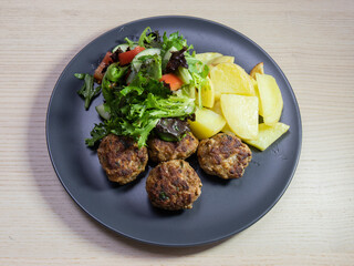 A plate of pork meatball, baked potato, and green salad.