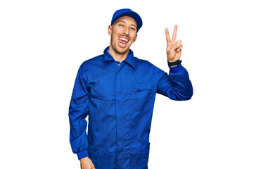 Fototapeta na wymiar Bald man with beard wearing builder jumpsuit uniform smiling with happy face winking at the camera doing victory sign with fingers. number two.