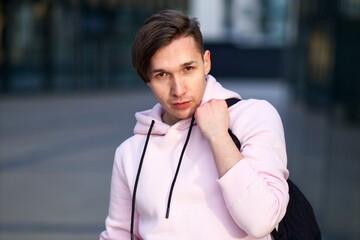 Portrait of handsome young university or college student in pink hoodie with backpack outdoors