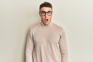 Hispanic young man wearing casual turtleneck sweater afraid and shocked with surprise and amazed expression, fear and excited face.