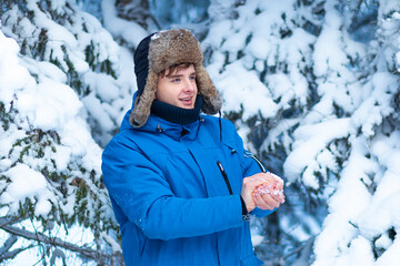 Happy young positive man is playing in snowball game in the winter snowy forest, smiling, having fun outdoors with snow