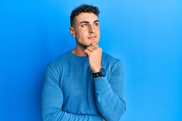 Hispanic young man wearing casual winter sweater with hand on chin thinking about question, pensive expression. smiling with thoughtful face. doubt concept.