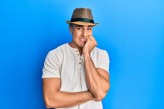 Hispanic young man wearing summer hat looking stressed and nervous with hands on mouth biting nails. anxiety problem.